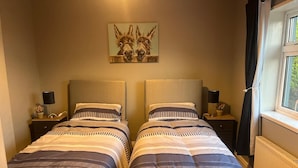 A double bed room with striped bedding, two bedside tables with lamps, a painting of donkeys on the wall, and a window with curtains. - Welcoming 3-bedroom cottage with WiFi in Cork (Cork)