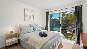 Un dormitorio con cama, mesitas de noche, ventana con cortinas y una vista al exterior, además de un cuadro en la pared.