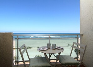 A balcony with a table and chairs overlooking a beach. - Studio with sea view (Canet-en-Roussillon)