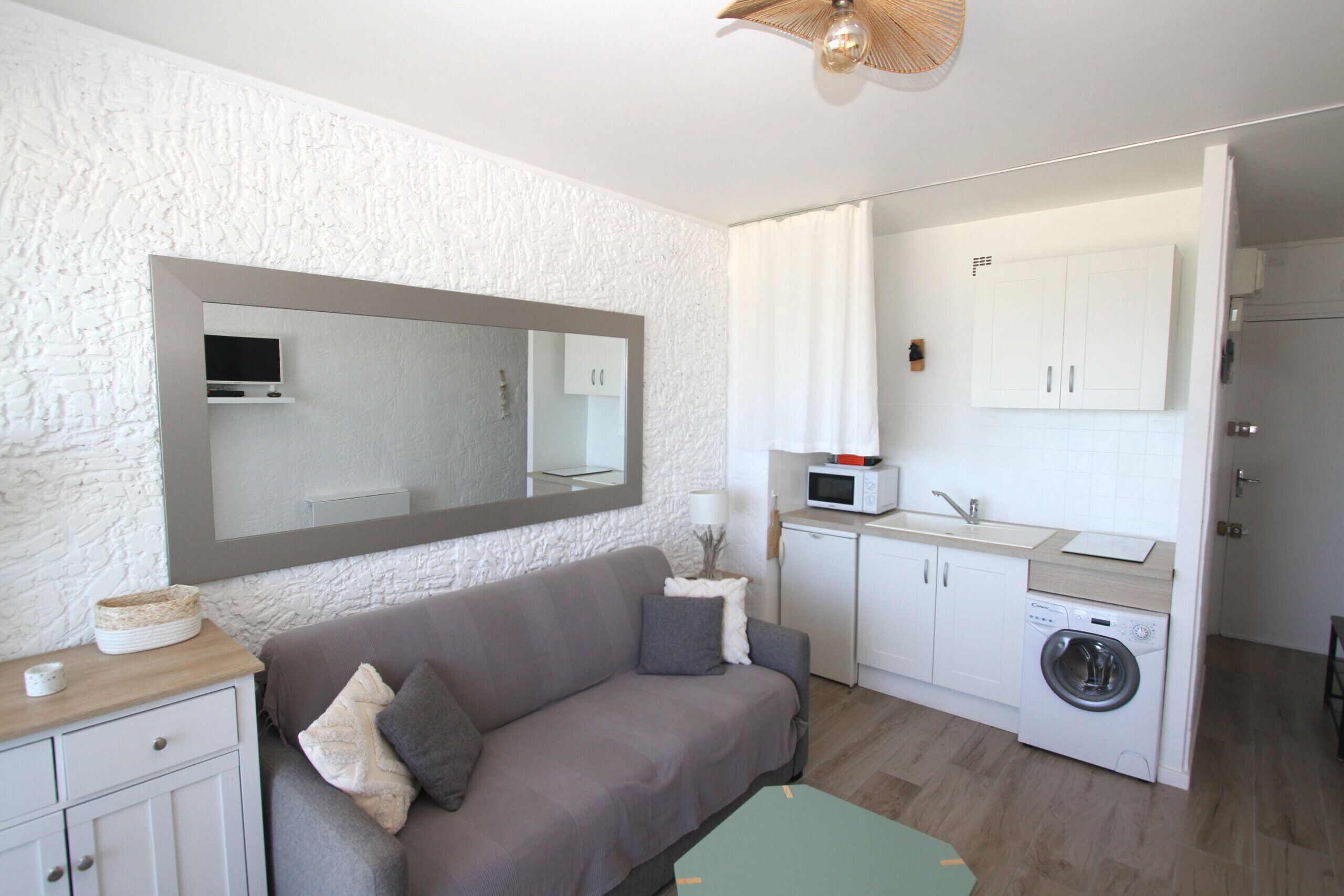 Un espace de vie compact comprenant un canapé, un lave-linge, un four à micro-ondes et un grand miroir.