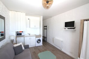 A compact living space with a sofa, a washing machine, a microwave, and a TV mounted on the wall. - Studio with sea view (Canet-en-Roussillon)