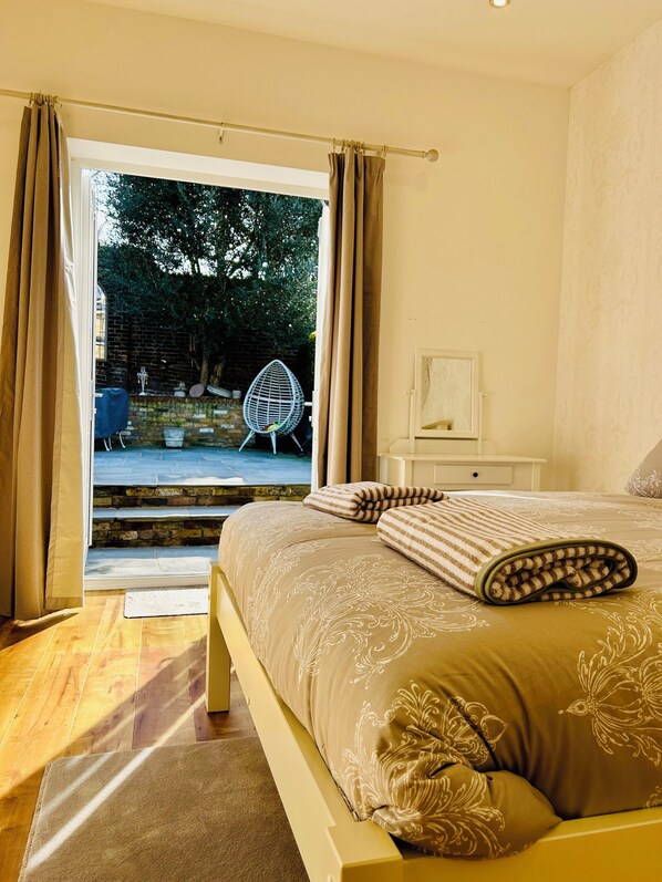 A bedroom with a large bed, a nightstand, and a chair outside the window.