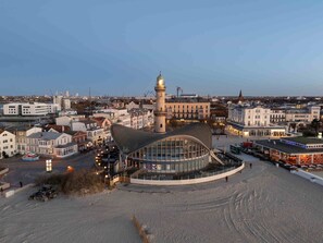 A coastal cityscape with a prominent tower, a modern building with a curved roof, and a waterfront promenade. - CBlue "Möwe" in Hohe Düne (Rostock)
