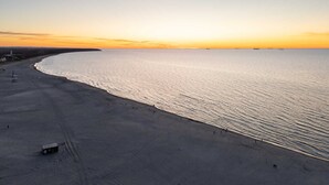 Una playa con cielo despejado, orilla de arena y algunas personas caminando cerca del agua.