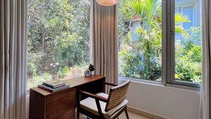 A room with a desk, chair, and large windows offering a view of greenery. - SolVanya by evaddo stays (Siolim)