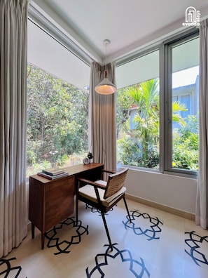 Habitación con escritorio, silla y ventanas amplias que dan a vistas de vegetación.