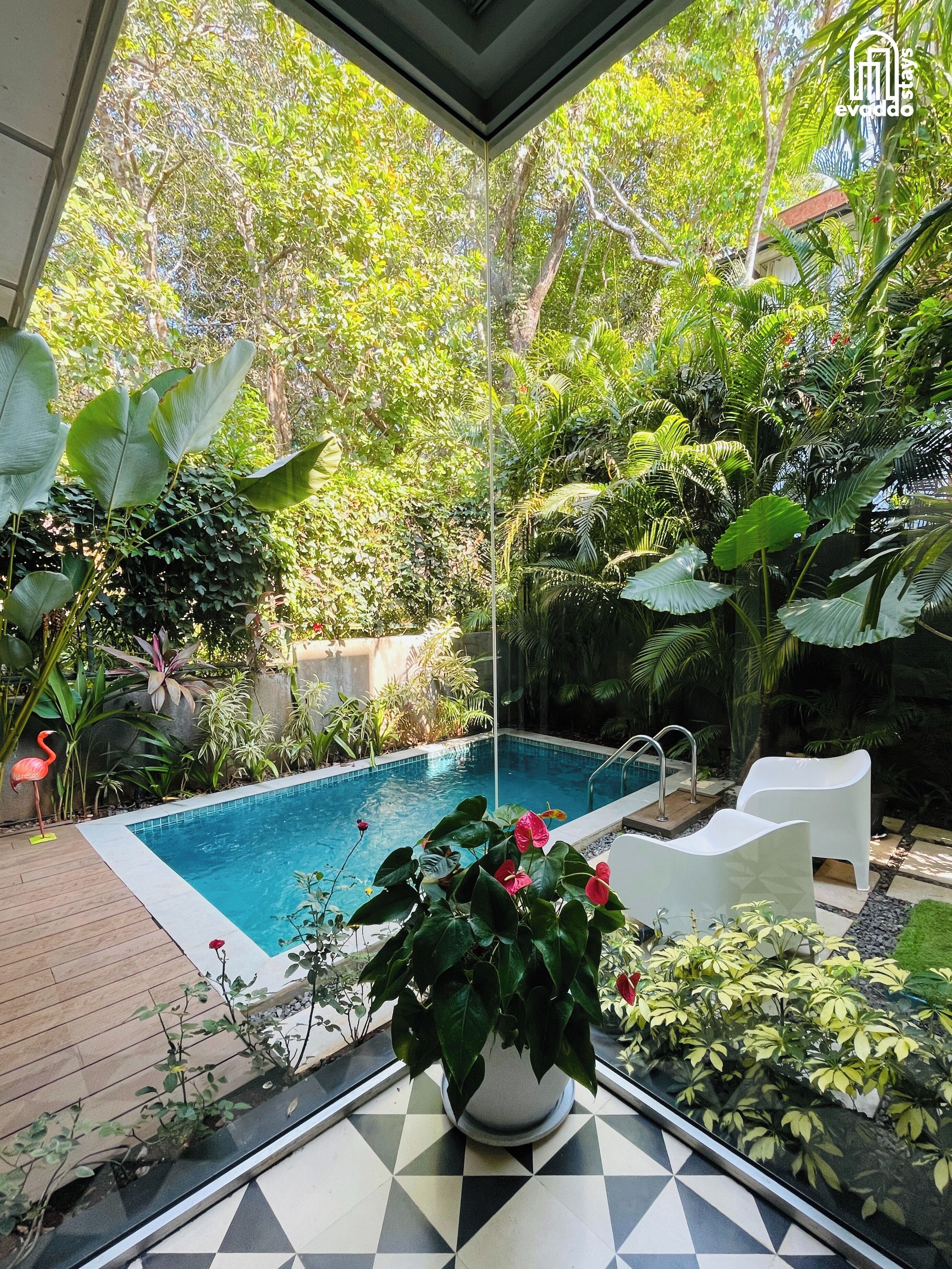 Ein Pool, umgeben von üppigem Grün, einer Flamingo-Statue und einem Topf mit rosa Blüten.