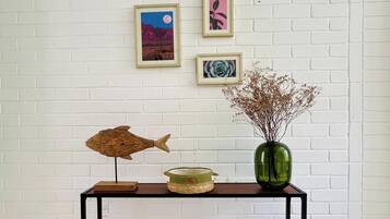 A console table with a fish sculpture, a vase with dried flowers, and framed artwork on a white brick wall.