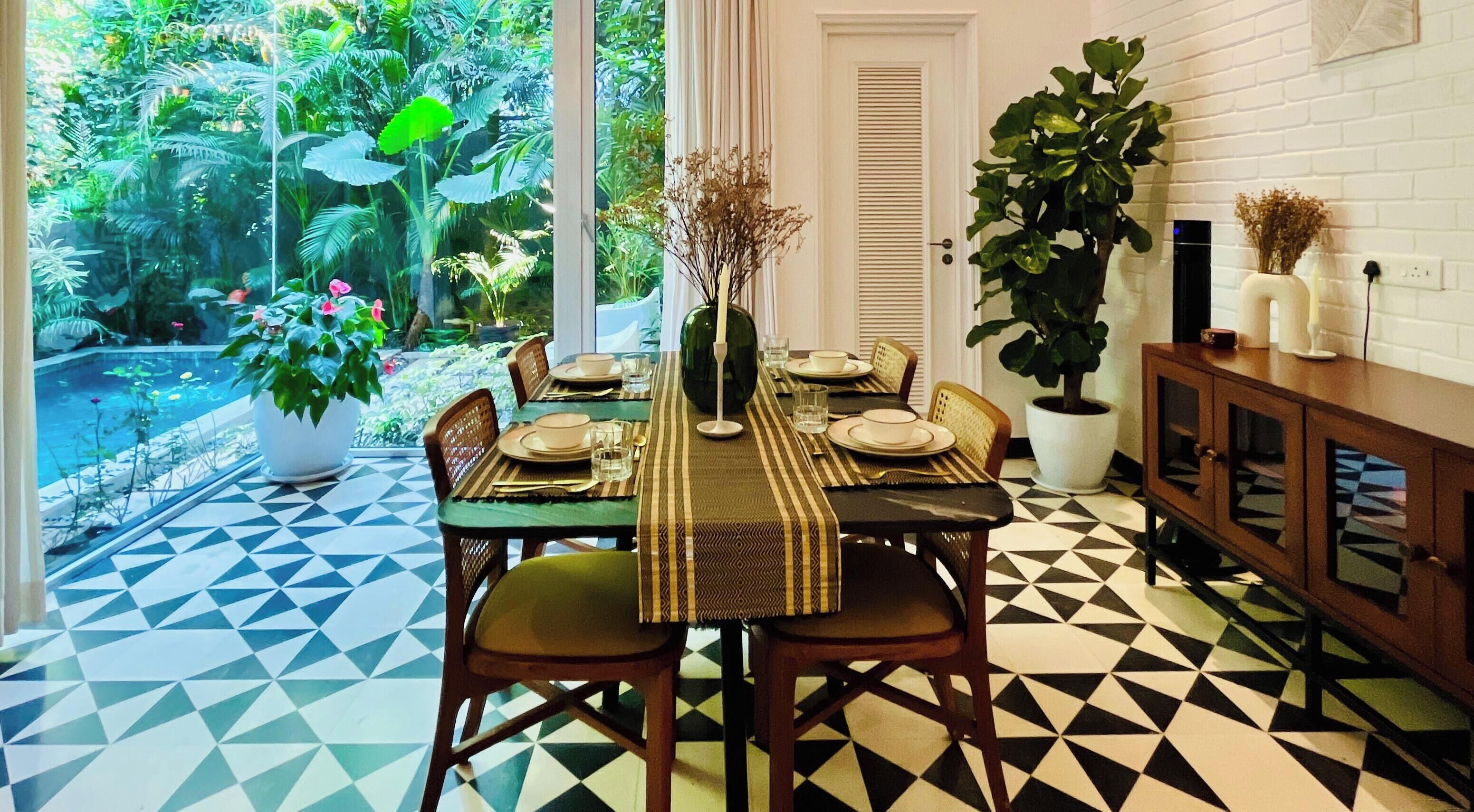 A dining area with a geometric patterned floor, a table set for four, and a view of a lush garden through a glass door.