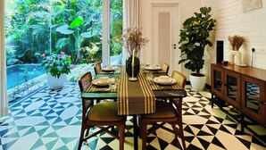 A dining area with a geometric patterned floor, a table set for four, and a view of a lush garden through a glass door. - SolVanya by evaddo stays (Siolim)