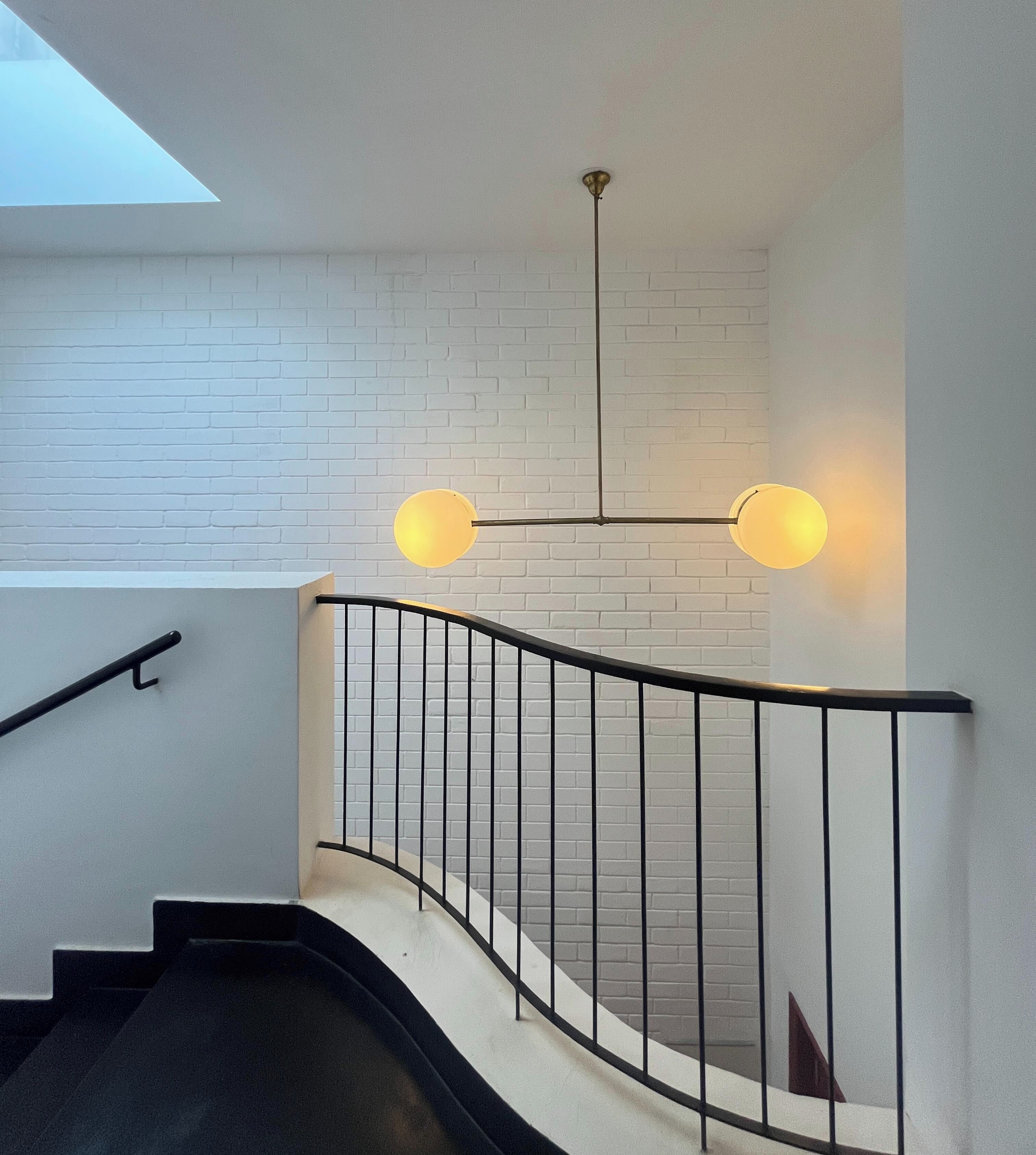 Escadaria com corrimão de metal preto, paredes de tijolos brancos e duas luminárias fixadas na parede.