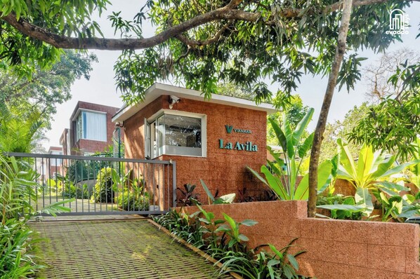 Un edificio con un letrero que dice 'Vianaar La Avila', rodeado de exuberante follaje y una entrada con portón.