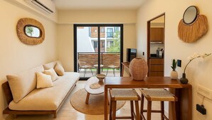 A modern living room with a sofa, a dining table with two chairs, a TV, and a large window with a view of buildings. - Modern 2BR Tulum Rooftop  Pool  Gym Coworking WiFi (Tulum)