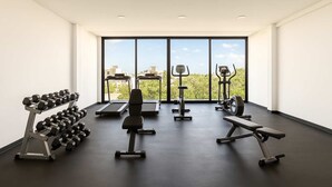 A modern gym with exercise equipment, large windows, and a view of buildings and trees. - Modern 2BR Tulum Rooftop  Pool  Gym Coworking WiFi (Tulum)