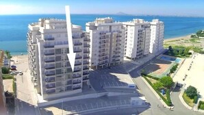 A high-rise residential building with multiple balconies, a parking area, and a view of the sea. - 2 bedroom apartment / lmb1323 (La Manga Del Mar Menor)