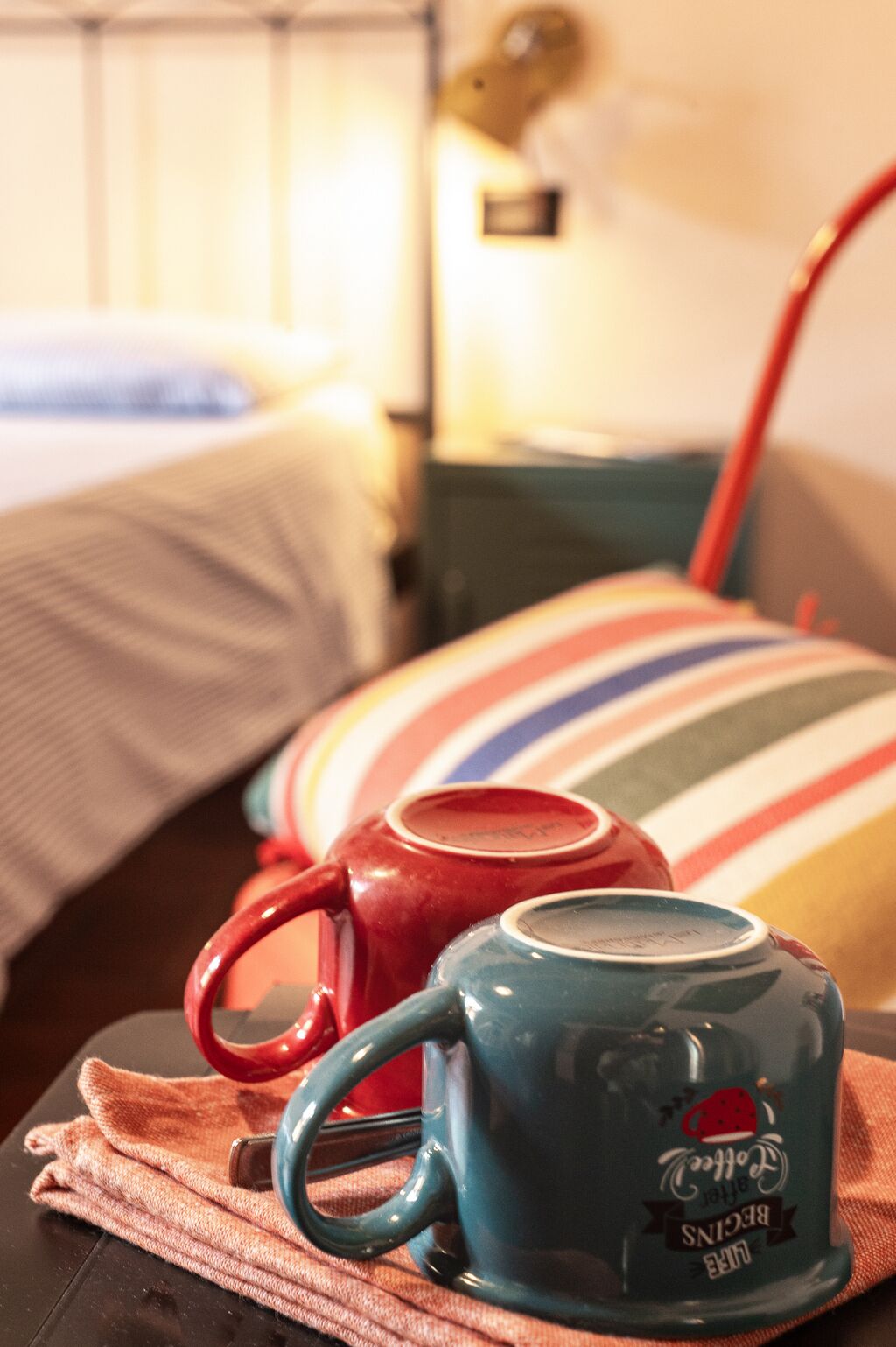 Una cama con dos tazas, un almohadón a rayas y una lámpara en una habitación de hotel.