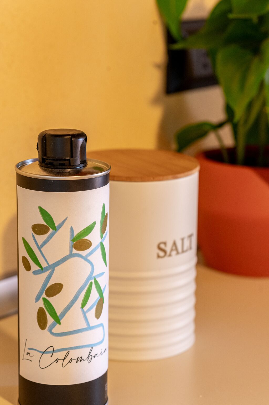 Eine schwarz-weiße Thermoskanne mit farbigem Dekor und der Aufschrift "La Colombina", platziert auf einem Tisch neben einem weißen Behälter mit dem Schriftzug "SALT".