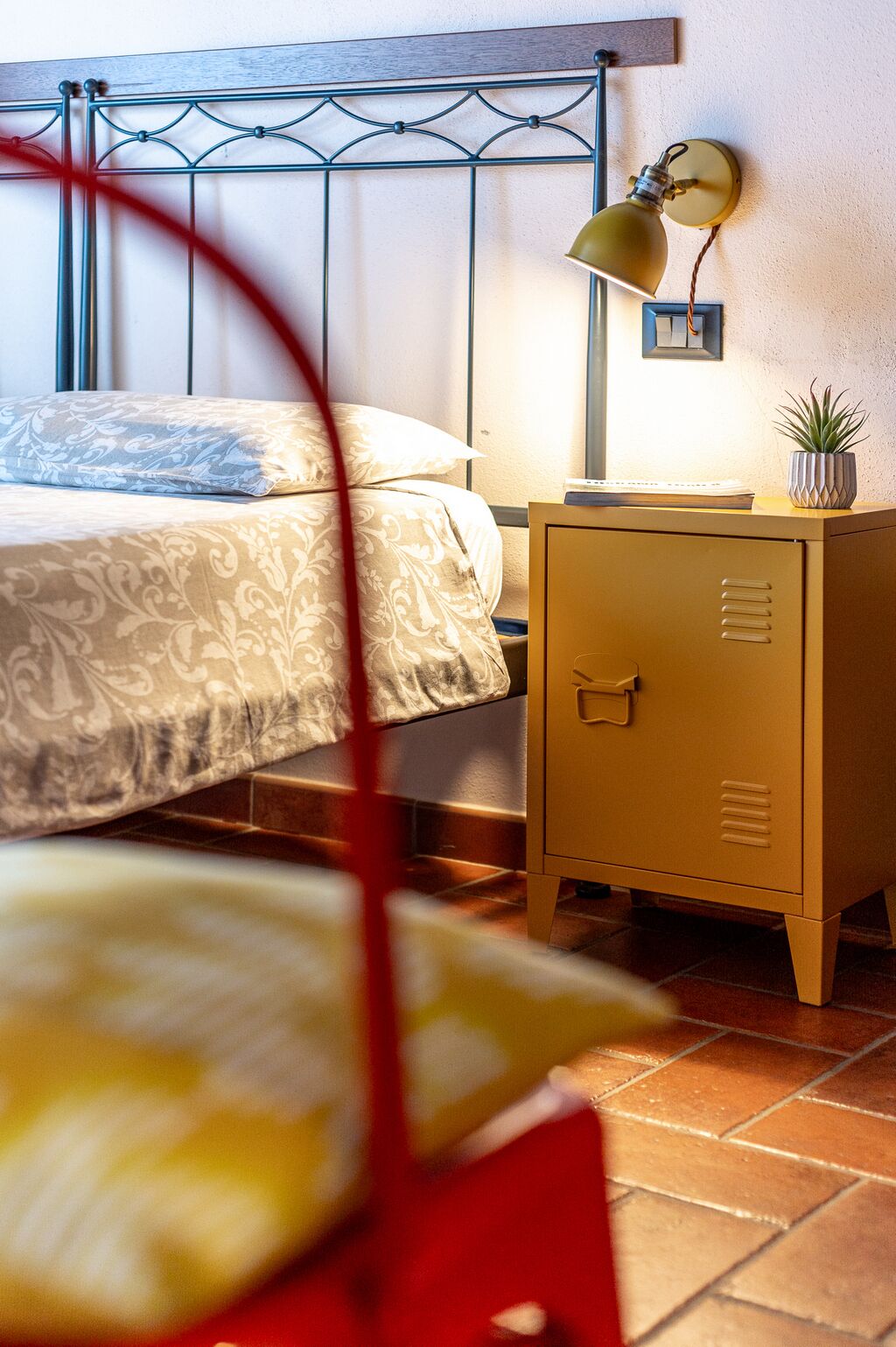Een slaapkamer met een bed, een bedlampje, een nachtkastje en een kleine potplant.