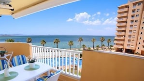 A balcony with a view of the sea, a pool, and a building.