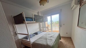 A room with a bunk bed, a balcony with a chair, and a ceiling fan.