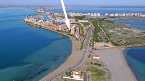 An aerial view of a coastal city with a prominent white skyscraper, a marina, and residential buildings along the waterfront.