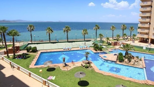 A hotel with a pool area, palm trees, and a view of the ocean.