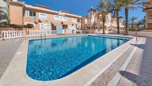 Une piscine dotée d’une terrasse carrelée, entourée de bâtiments avec balcons et de palmiers.
