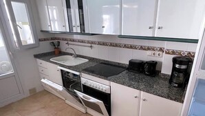 Une cuisine avec des meubles blancs, un plan de travail en granit, un lave-vaisselle encastré, une machine à café et un grille-pain.