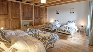 A room with wooden beams, two beds with patterned bedding, a shelf with books, and a small table with a lamp. - Renovated country house, ideal for 10, natural setting and modern comfort (Gumières)