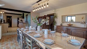 Una cocina amplia con una larga mesa de comedor preparada para seis personas, equipada con electrodomésticos modernos y una lámpara colgante en el centro.
