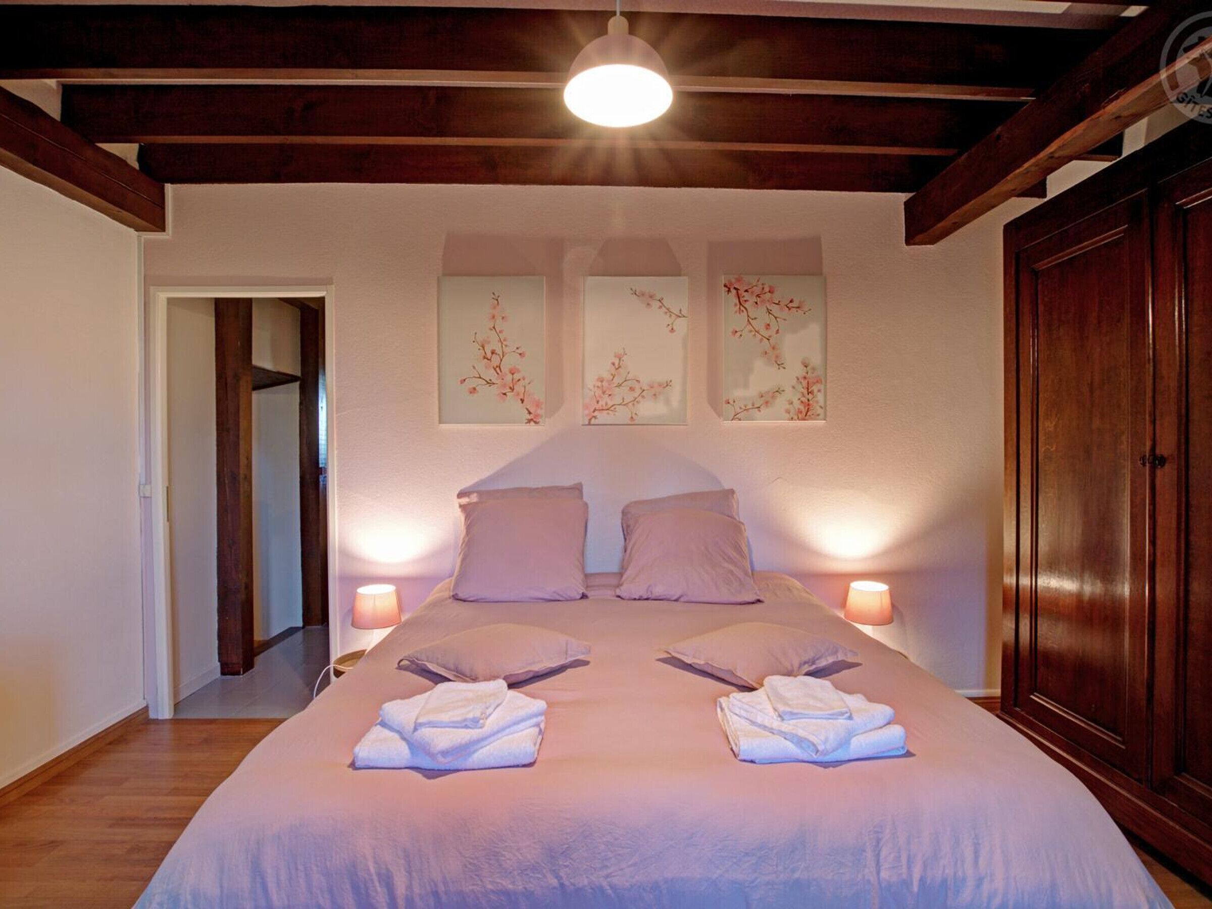 A bedroom with a large bed, two bedside tables, and three wall-mounted pictures.