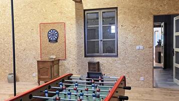 A room with a foosball table, a dartboard, and a window with blinds.