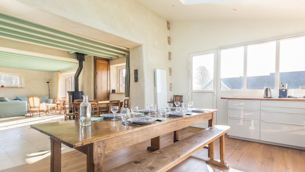 A spacious living area with a wooden dining table set for four, a kitchen with white cabinets, and a large window providing a view of the outdoors.
