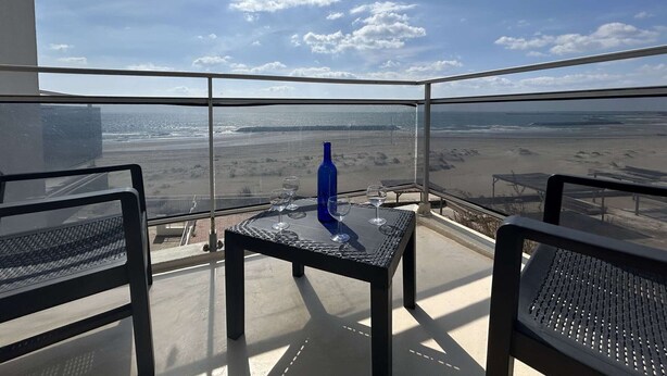 Un balcon avec une table et des chaises donnant sur une plage.
