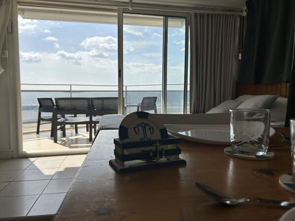 A room with a view of the sea, a dining table with a plate, a glass, and a small decorative item.