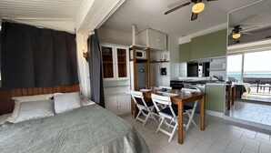 Une chambre avec un lit, un coin repas avec une table et des chaises, une kitchenette équipée d’un four à micro-ondes et d’une cuisinière, et une vue sur la mer.