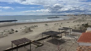 Une plage avec un rivage sablonneux, une jetée et quelques bâtiments en arrière-plan.