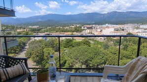 Un balcón con vistas a un pueblo, una mesa con una botella y una silla.