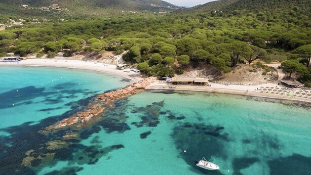Zona costera con aguas turquesas cristalinas, un barco y una playa con edificios y árboles.