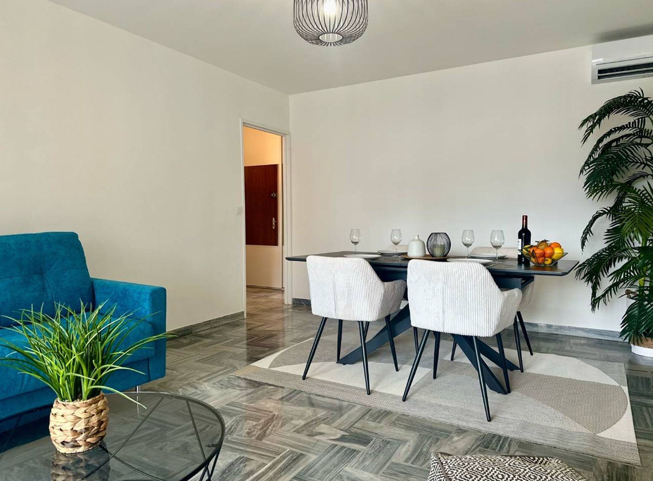 A modern living room with a blue sofa, a dining area with a table set for four, and a large potted plant.