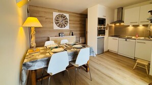 A compact kitchen with white cabinets, a microwave, oven, and dishwasher. There's a dining table set with plates, glasses, and a lamp. - Autrans - Renovated 6 pers apartment, 2 bedrooms, south terrace (Autrans-Méaudre en Vercors-Autrans)