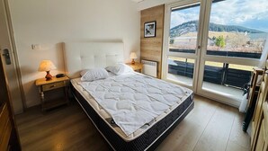 A bedroom with a bed, two bedside tables with lamps, a wooden headboard, a framed picture on the wall, and a large window with a view of a snowy landscape. - Autrans - Renovated 6 pers apartment, 2 bedrooms, south terrace (Autrans-Méaudre en Vercors-Autrans)