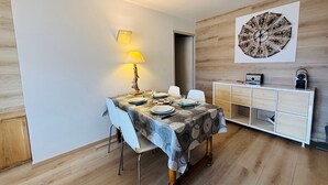 A dining area with a table set for four, a lamp, and a wall clock. - Autrans - Renovated 6 pers apartment, 2 bedrooms, south terrace (Autrans-Méaudre en Vercors-Autrans)