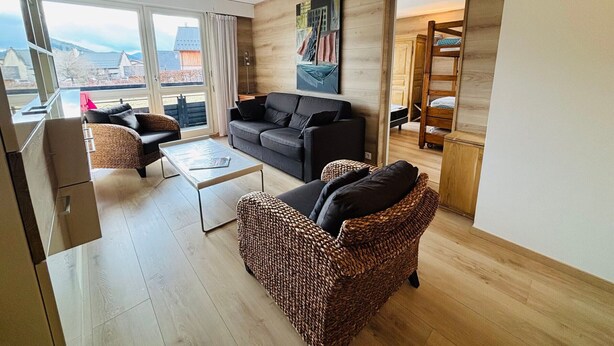 A modern living room with a sofa, a wicker chair, a coffee table, and a bunk bed in the background. - Autrans - Renovated 6 pers apartment, 2 bedrooms, south terrace (Autrans-Méaudre en Vercors-Autrans)