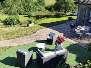Eine Terrasse mit Gartenmöbeln, einem Grill und Blick auf einen Teich.