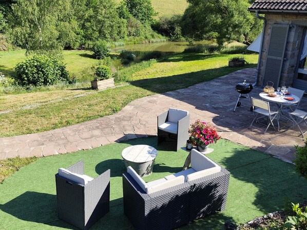 A patio area with outdoor furniture, a grill, and a view of a pond.