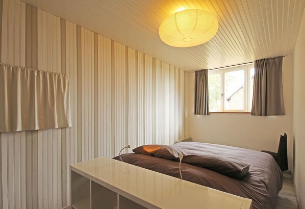 A bedroom with a bed, a bedside table, a hanging light fixture, and a window with curtains.