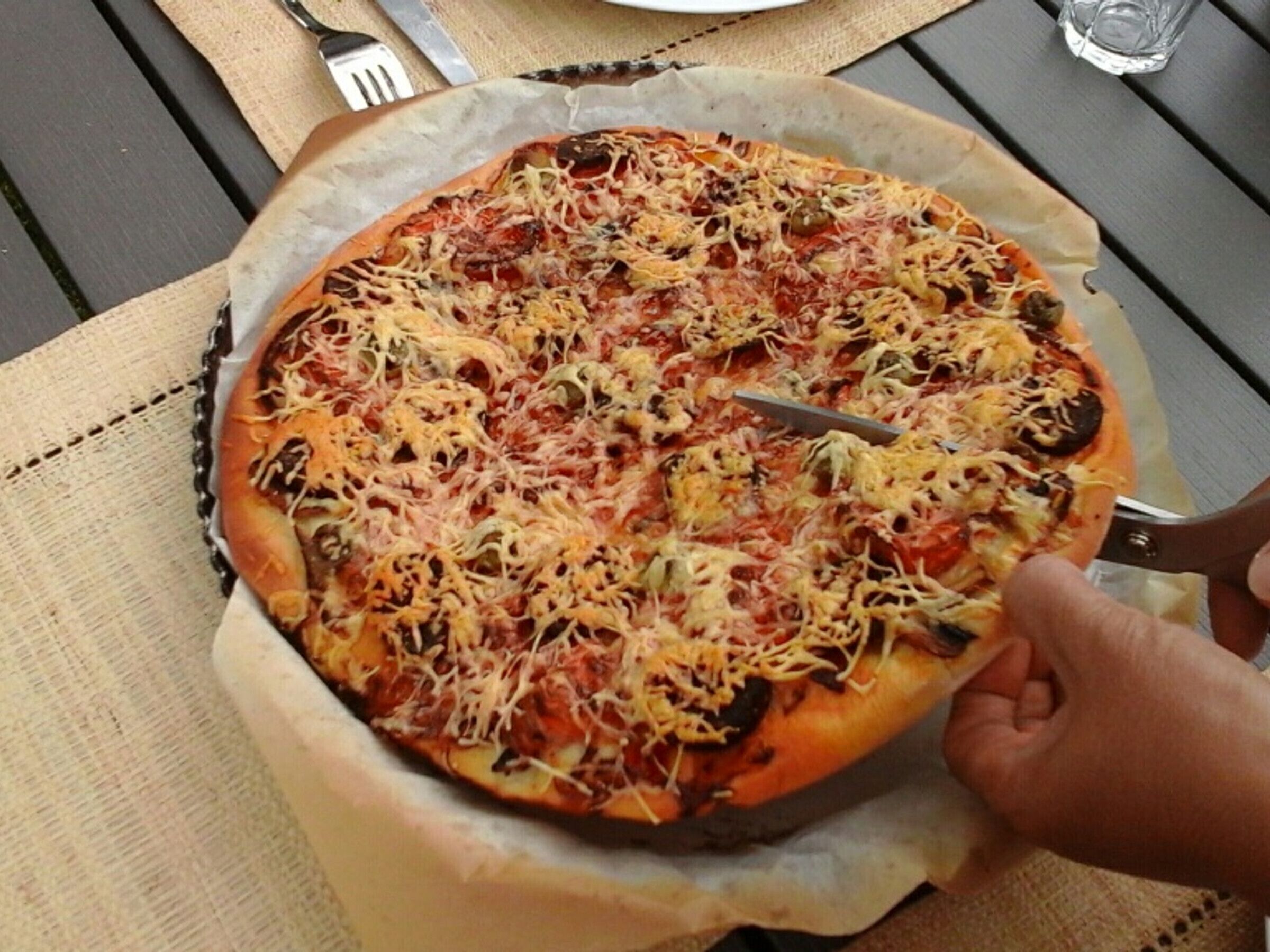Een pizza op een tafel, met een vork en mes ernaast.
