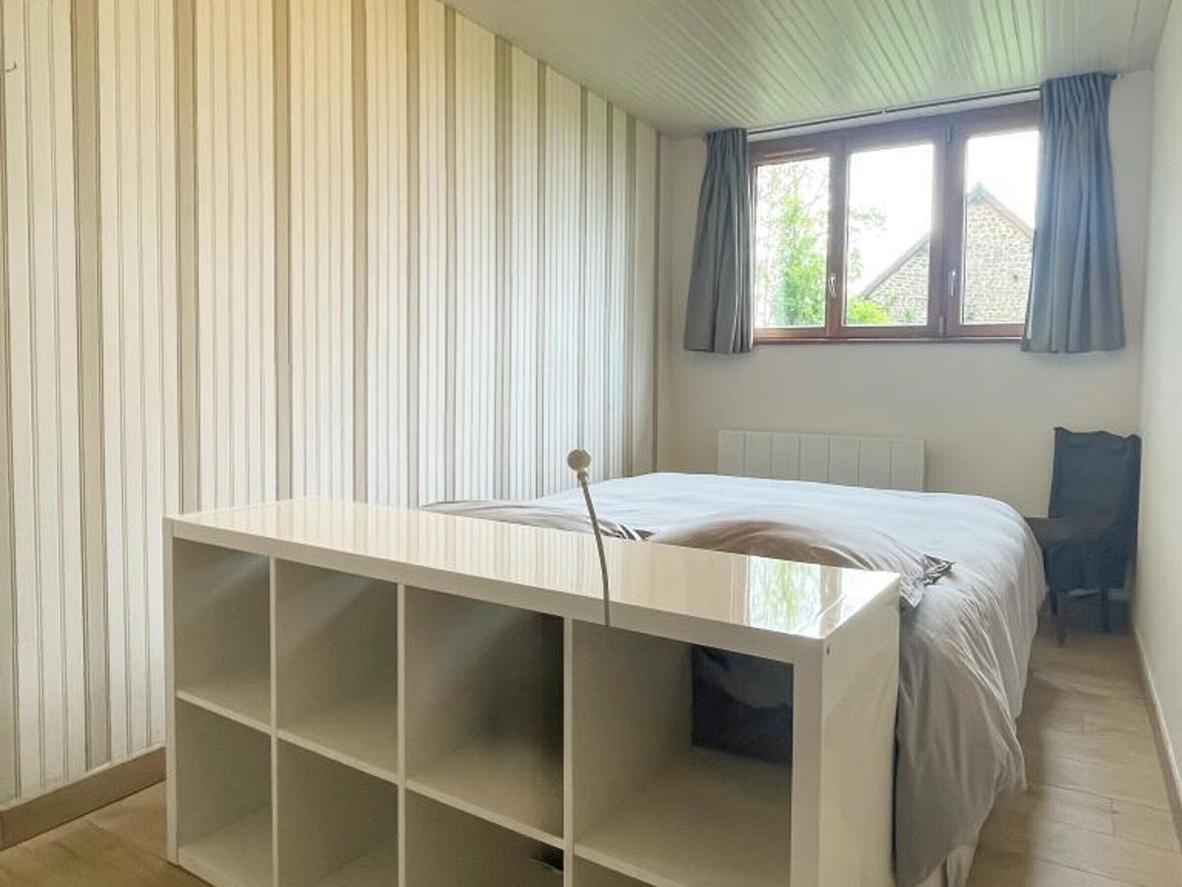 Ein Schlafzimmer mit Bett, einem Fenster mit Vorhängen, einem Heizkörper und einem weißen Stauraum.