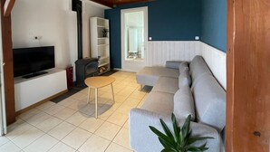 A living room with a wooden ceiling, a grey sofa, a TV, a small table, and a bookshelf. - Rustic cottage in Vendée Marshes, near beaches (Sallertaine)